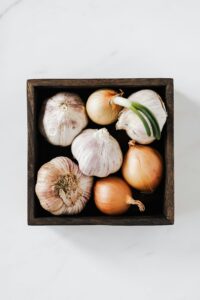 Aerial shot of fresh garlic and onion arranged in a wooden box, showcasing organic ingredients.