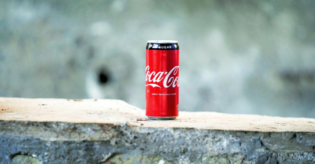 A can of Coca Cola placed on a rough concrete surface with a blurred background.